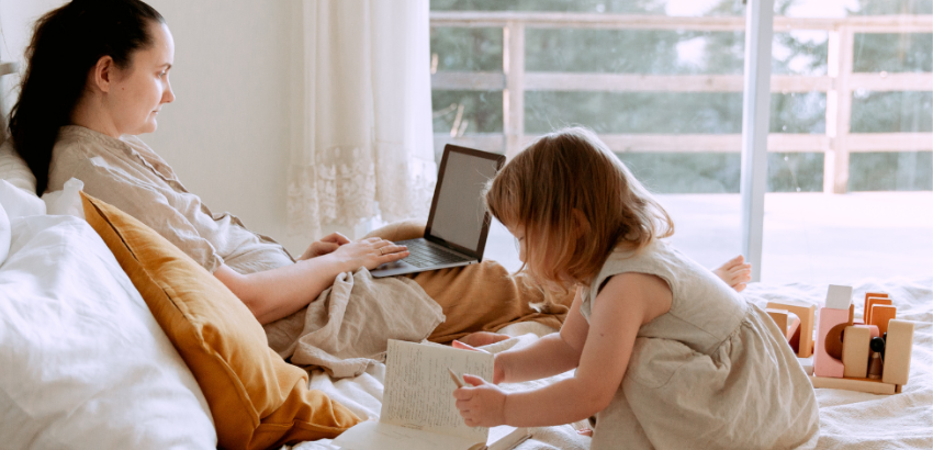 Single Parent preparing her family budget while her child plays beside her on the bed